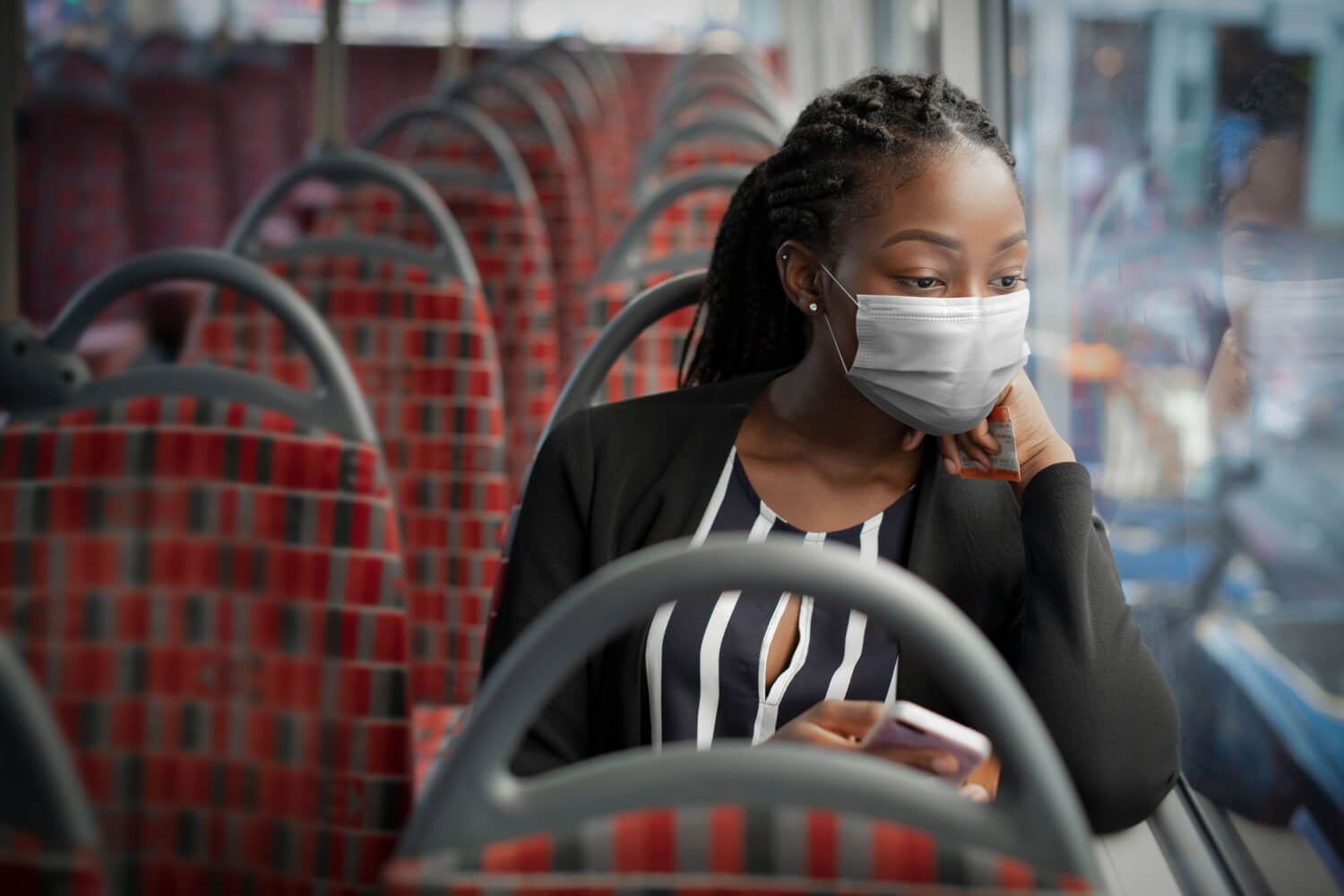Mulher sentada em ônibus fretado com a mão no queixo e usando máscara facial